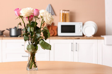 Vase with beautiful rose flowers on wooden table in kitchen