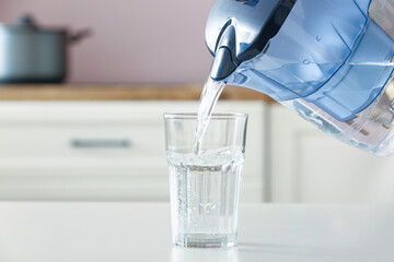 Pouring of water from filter jug into glass on table in kitchen © Pixel-Shot