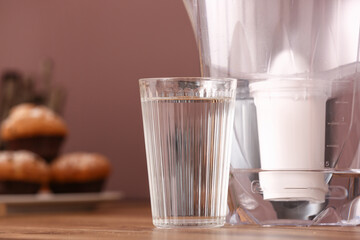 Glass of pure water and filter jug on wooden kitchen counter