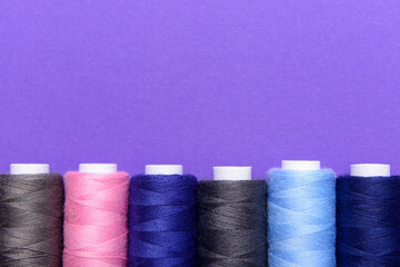 Set of different thread spools on purple background, closeup