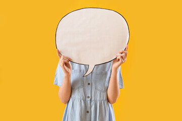 Young woman hiding face behind blank speech bubble on yellow background