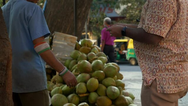 Tender coconut water seller and buyer exchanging money, cash, and currency in the marketplace during a transaction, India