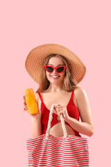 Beautiful young woman with sunscreen cream and beach bag on pink background