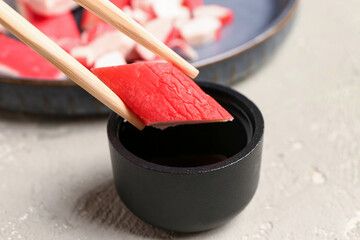 Putting piece of tasty crab stick into bowl with sauce on light background, closeup © Pixel-Shot
