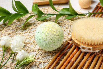 Bath bomb with massage brush, roses and plant branch on mat, closeup