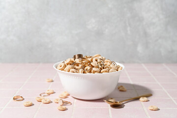 Bowl with cereal and golden rings on pink tile table