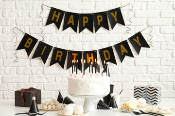 Birthday cake with candles on white table and garlands on brick wall