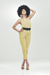 Shes a disco diva. Full length shot of young woman wearing a 70s retro jumpsuit striking a pose in...