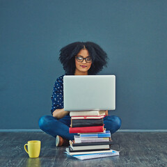 A grades only for her. Studio shot of a young woman using a laptop with books stacked in front of her against a gray background.