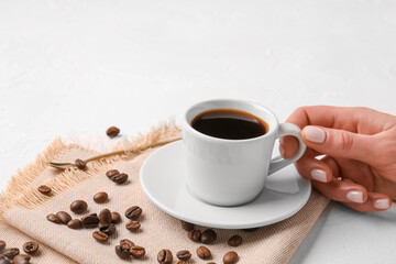Female hand with cup of coffee and beans on light background