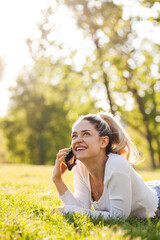 Beautiful girl lying in a field in the park. Talking on phone.