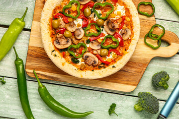 Board with vegetable pizza and ingredients on green wooden background