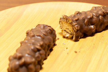 A chocolate and walnut covered nougat bar split in two on a wooden plate