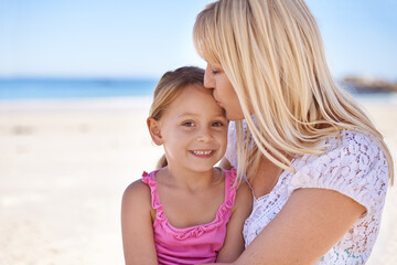 Mommys little girl. A loving mother giving her daughter a kiss on the forehead while at the beach.