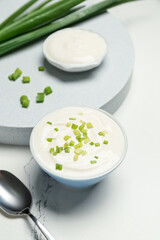 Bowl of tasty sour cream with green onion on white marble background