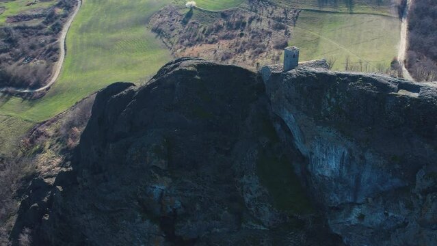 Aerial footage of Pietra Perduca, volcanic rock, church set at top stone immersed in countryside landscape, cultivated land in Val Trebbia Bobbio, Emilia Romagna, Italy