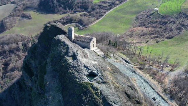 Aerial footage of Pietra Perduca, volcanic rock, church set at top stone immersed in countryside landscape, cultivated land in Val Trebbia Bobbio, Emilia Romagna, Italy