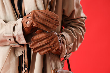 Beautiful young woman wearing leather gloves and coat on red background, closeup