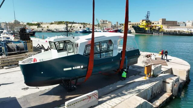 Drone aerial shot flying towards a boat lifted in air while workmen are checking lifting straps around it at MMH ship yard Malta