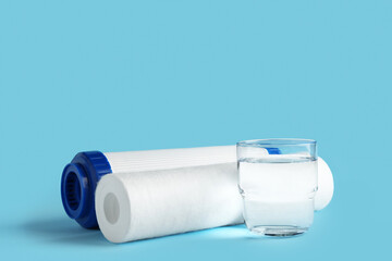 Glass of liquid and water filter cartridges on blue background