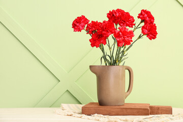 Vase with red carnations on white wooden table near light green wall