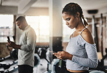 Fitness facilitated with smart apps. a young woman using a mobile phone in a gym.