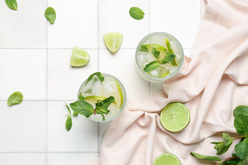 Glasses of tasty mojito and ingredients on white tile background
