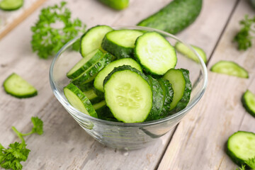 bowl with pieces of fresh cucumber on light wooden background