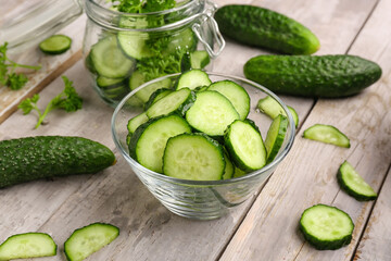 Bowl with fresh cut cucumbers on light wooden background