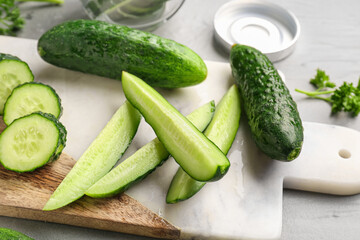 Board with fresh cut cucumbers on grey background