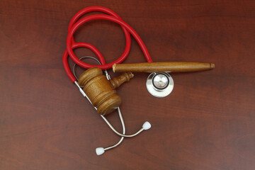 Broken wooden judge gavel and red stethoscope on table.