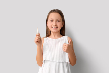 Little girl with chalk piece showing thumb-up on light background. Children's Day celebration