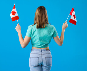 Young woman with flags of Canada on blue background, back view