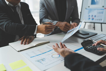 Confident group of business people pointing to graphs and charts to analyze market data, calculate balance sheet, account, net profit to plan new sales strategy to increase production capacity.