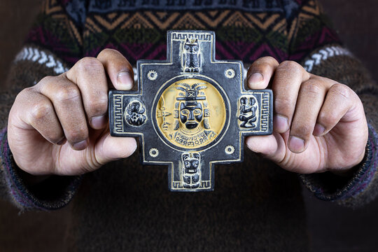 Indigenous man hold a chakana or Andean cross with the symbols of an Inca, toad, family, puma, owl. Culture and ancient history of Tiwanaku - Bolivia