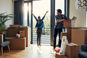 Hello there neighbors. a cheerful middle aged woman stretching her arms out on her balcony while her husband looks at her and packs out boxes on moving day.