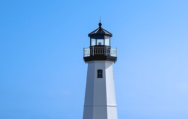 Lighthouse in daytime, centered against clear blue sky. Sky becomes a bit lighter, with a hint of clouds, on the right side. Fresh summer day. Copy space.