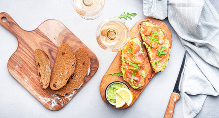 Gourmet lunch with avocado salmon toasts on rye bread and rose wine glasses, gray table background, top view