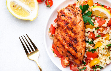 Grilled chicken fillet with bulgur tabbouleh salad with colorful tomatoes, parsley and lemon dressing, white table background, top view