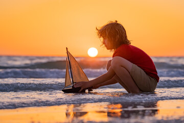 Little kid boy play with toy boat in the sea waves at the beach during summer vacation. Childhood and summer family vacation. Dream on travel. Travelling tour on sailing ship. Kids dream concept.