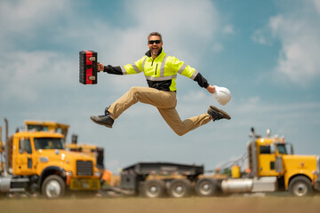 Construction builder excited jump in building uniform on buildings construction background. Builder at the construction site. Man worker with helmet on construction site. Bilder in hardhat. - obrazy, fototapety, plakaty