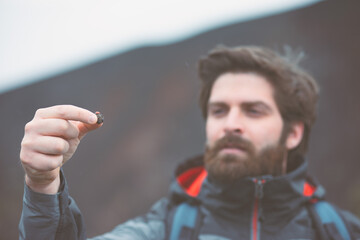 A young guy is holding a ladybug in the hand. The face is out of focus. 