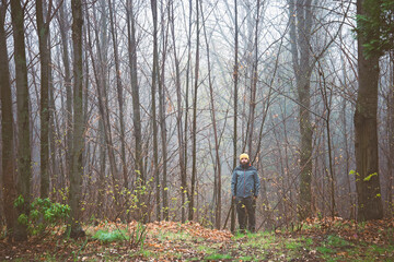 A young guy 30 y old with a yellow cap is walking in the forest. A subtle fog is in the wood. 