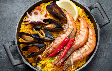 Traditional spanish seafood paella in the fry pan on a black background.