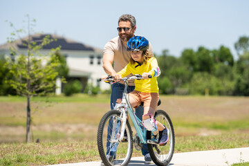 Obraz premium Father and son in a helmet riding bike. Little cute adorable caucasian boy in safety helmet riding bike with father. Family outdoors summer activities. Fathers day. Childhood and fatherhood.