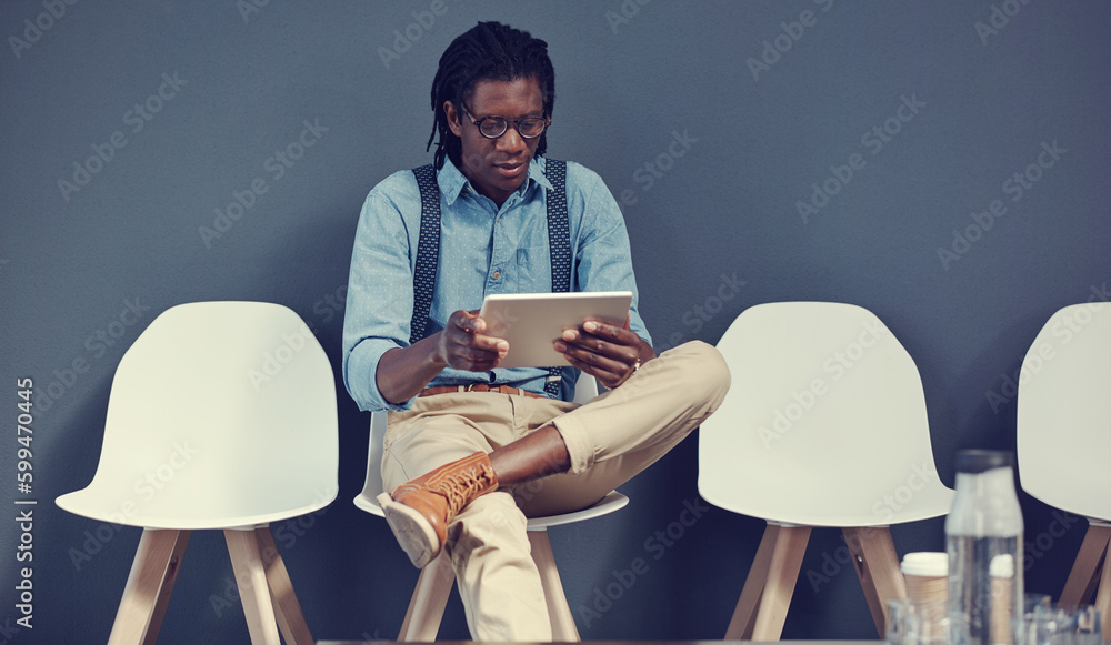 Poster Showing them how he uses all his time efficiently. a young businessman using a tablet while waiting for an interview.