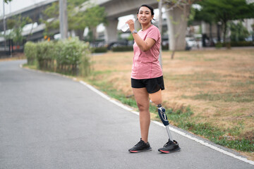 Exercise walking Asia woman with prosthetic leg and drink pure water in plastic bottle at the park city	