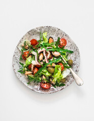 Salad with arugula, cherry tomatoes and seafood on a light background, top view
