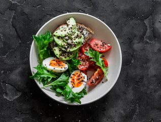 Healthy breakfast bowl - boiled egg, tomatoes, avocado cottage cheese seeds sandwich, green salad on a dark background, top view