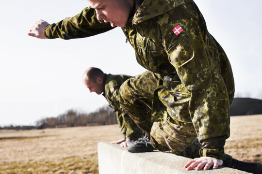 Soldier in training, military men and jump over a wall in obstacle course for fitness and endurance. Army team in camouflage uniform outdoor, train for war and exercise with mission and action